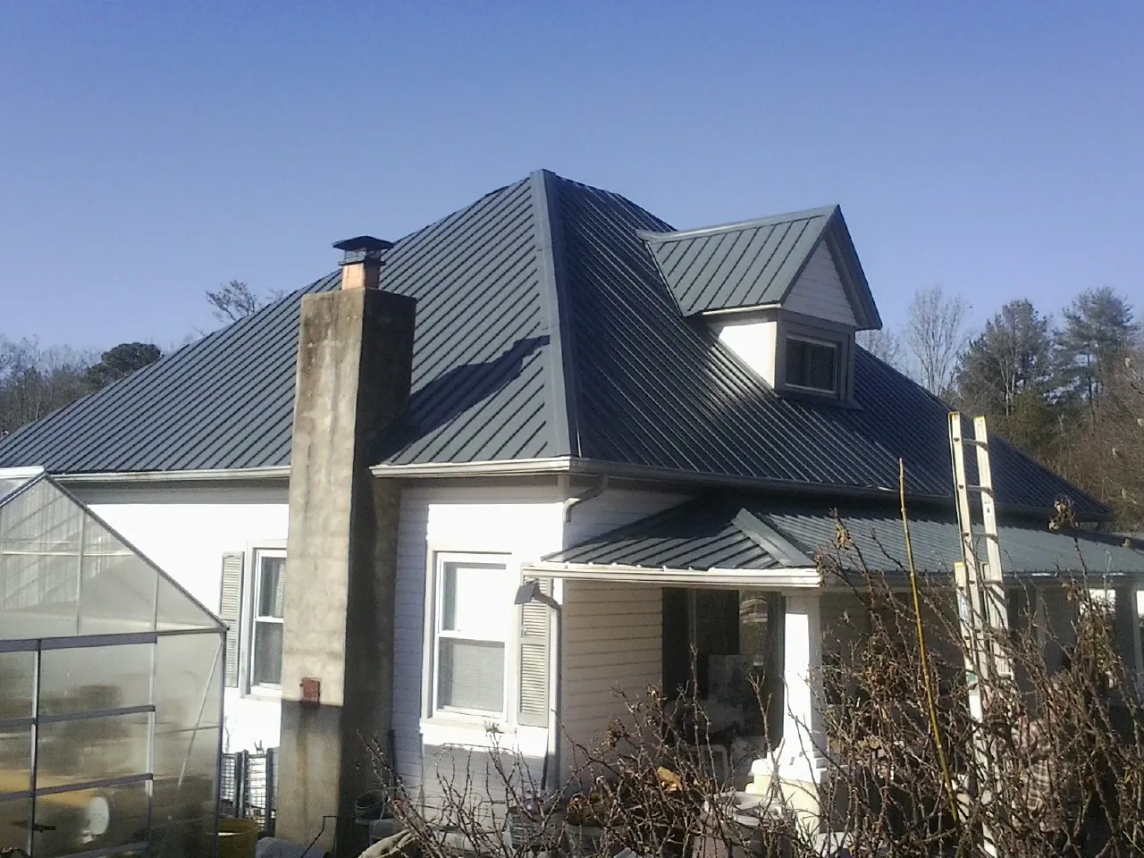 Dark blue standing seam metal roof on a white farmhouse with dormer — Slate & Tile Roof Repair by Roofing Brothers in Warfield