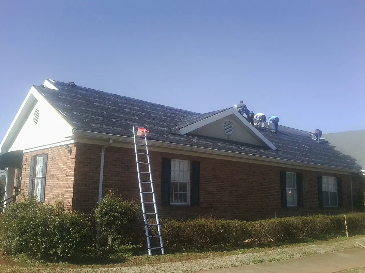 Crew tearing shingles off a brick ranch roof with a ladder set — Metal Roof Repair work by our crew in Warfield