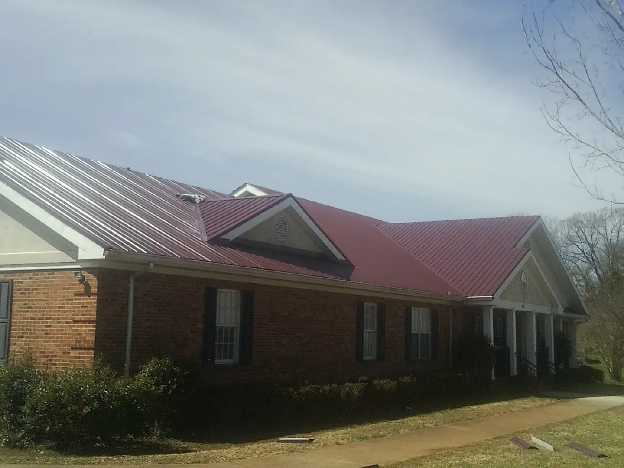 Red metal roof with gabled entries on a long brick building, from a Hail Damage Roof Repair job in Warfield