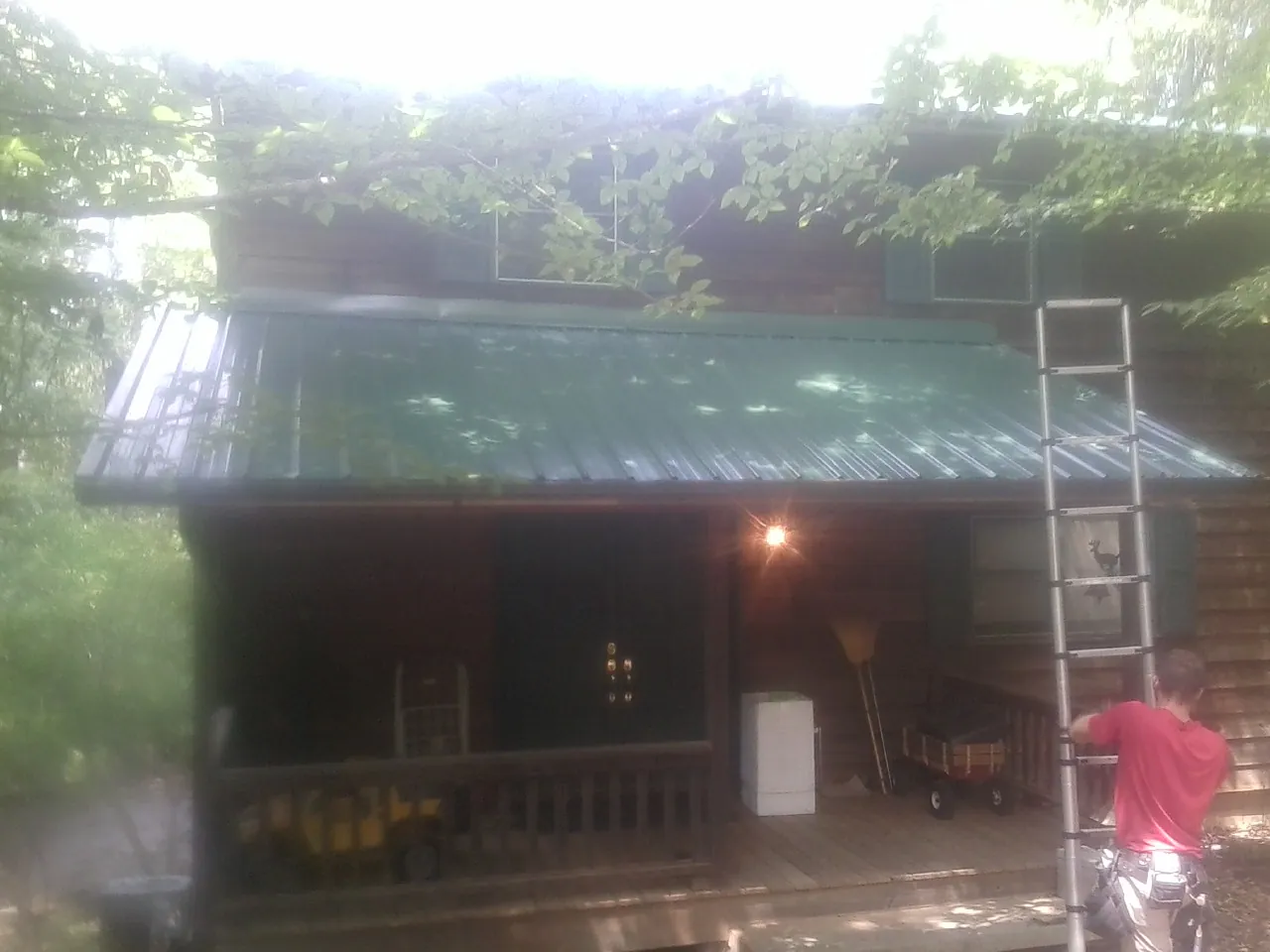 Worker on a ladder at the green porch roof of a wooded cabin in Warfield