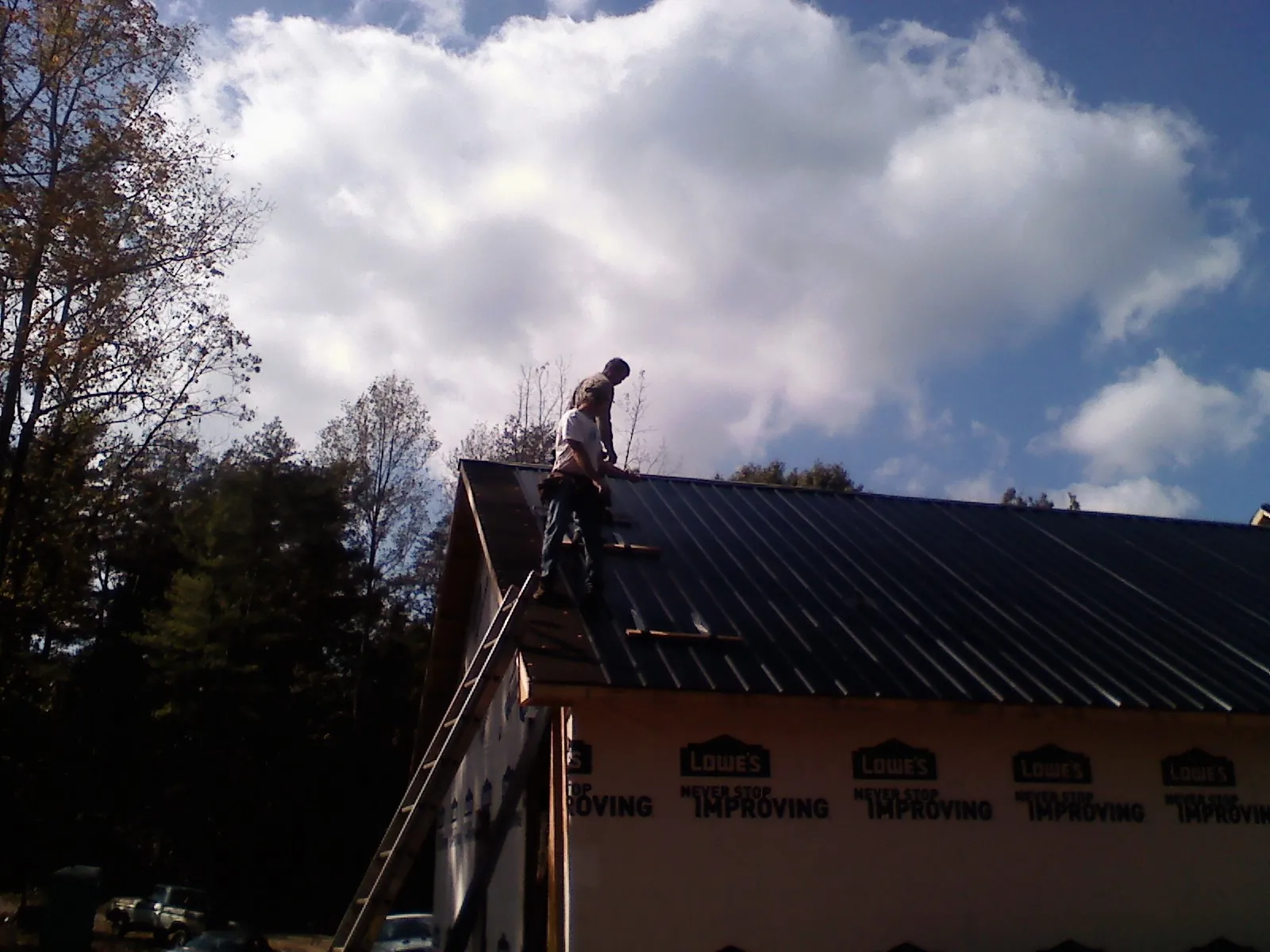 Roofer fastening dark metal panels high against a cloudy sky, from a Roof Inspection job in Warfield